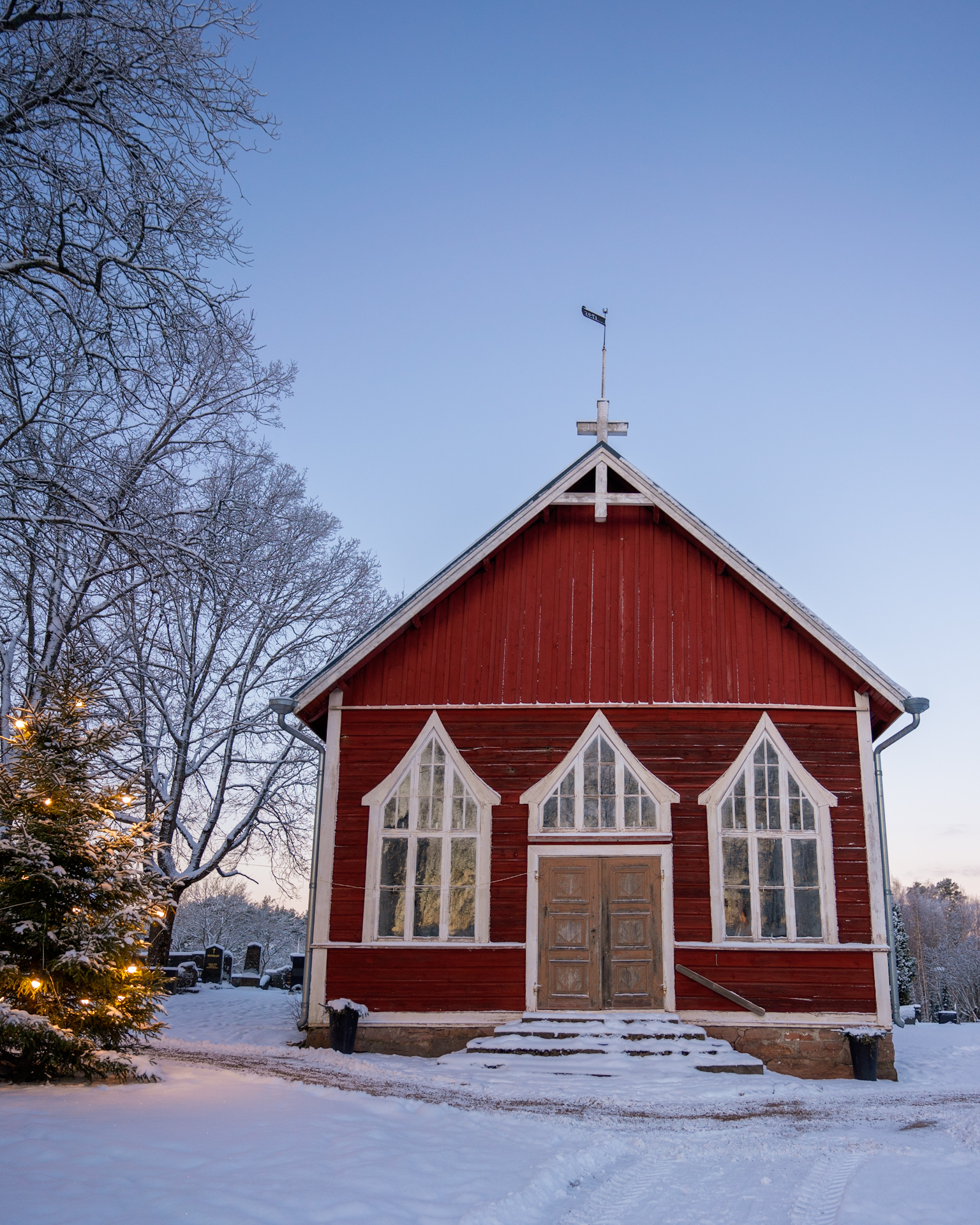 punainen kappeli ja valaistu joulukuusi lumisella hautausmaalla